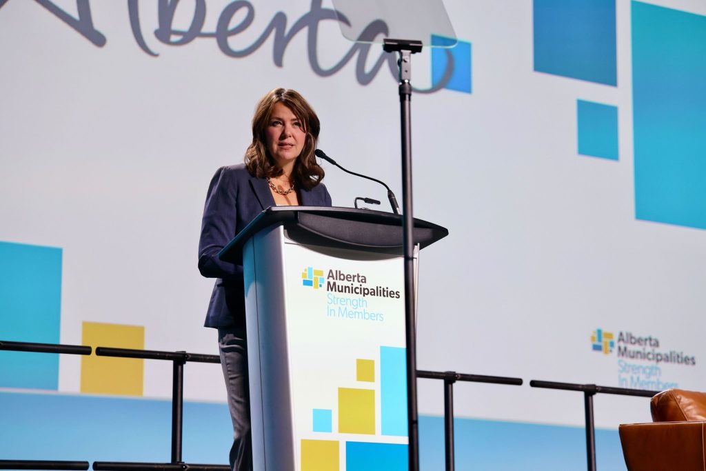 A woman stands confidently at a Podium Pros podium, addressing an audience in front of a large presentation screen.